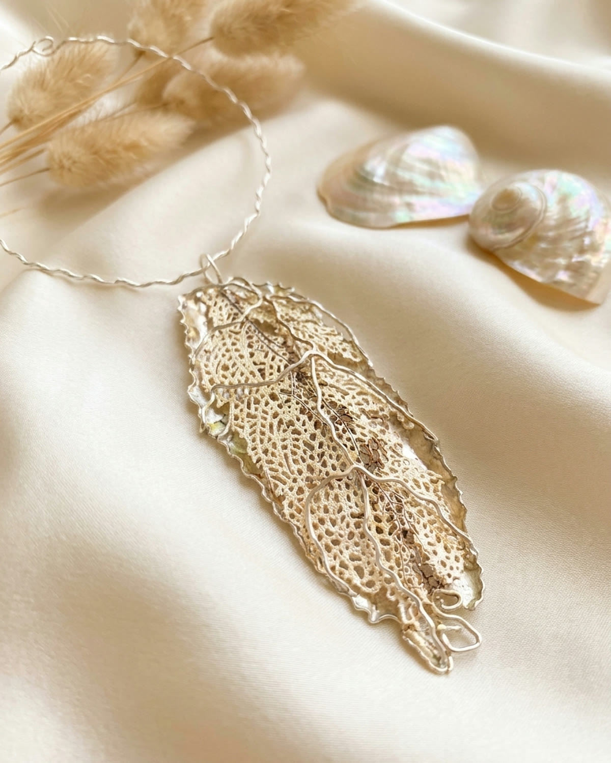 Leaf pendant necklace draped over ivory silk in soft heirloom light